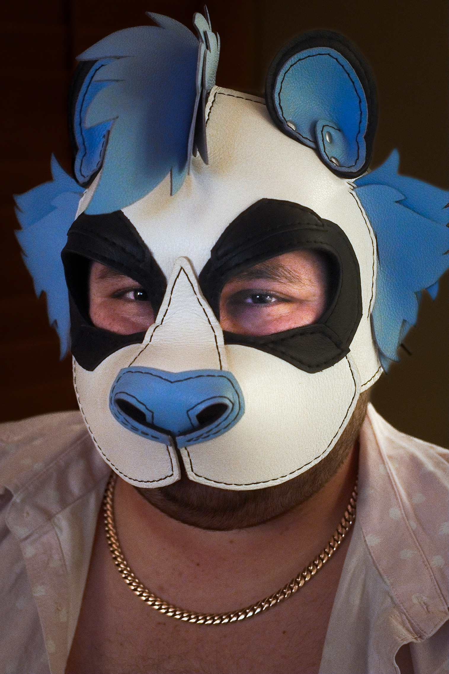 A portrait of myself, smiling, in my white and blue leather panda hood. I'm wearing a gold chain and a pink button-up shirt, left open.